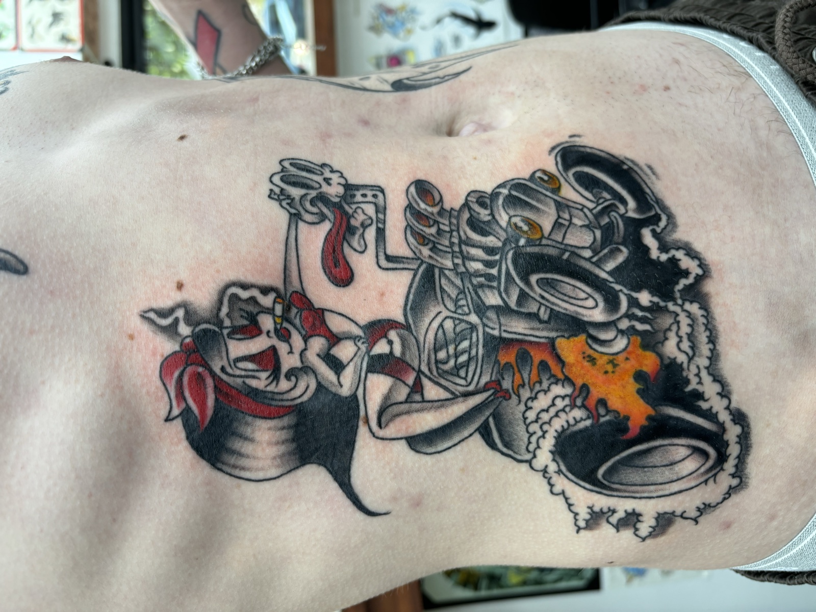 Hot rod chest piece — neo-traditional cartoon with flames, smoke, and a character behind the wheel